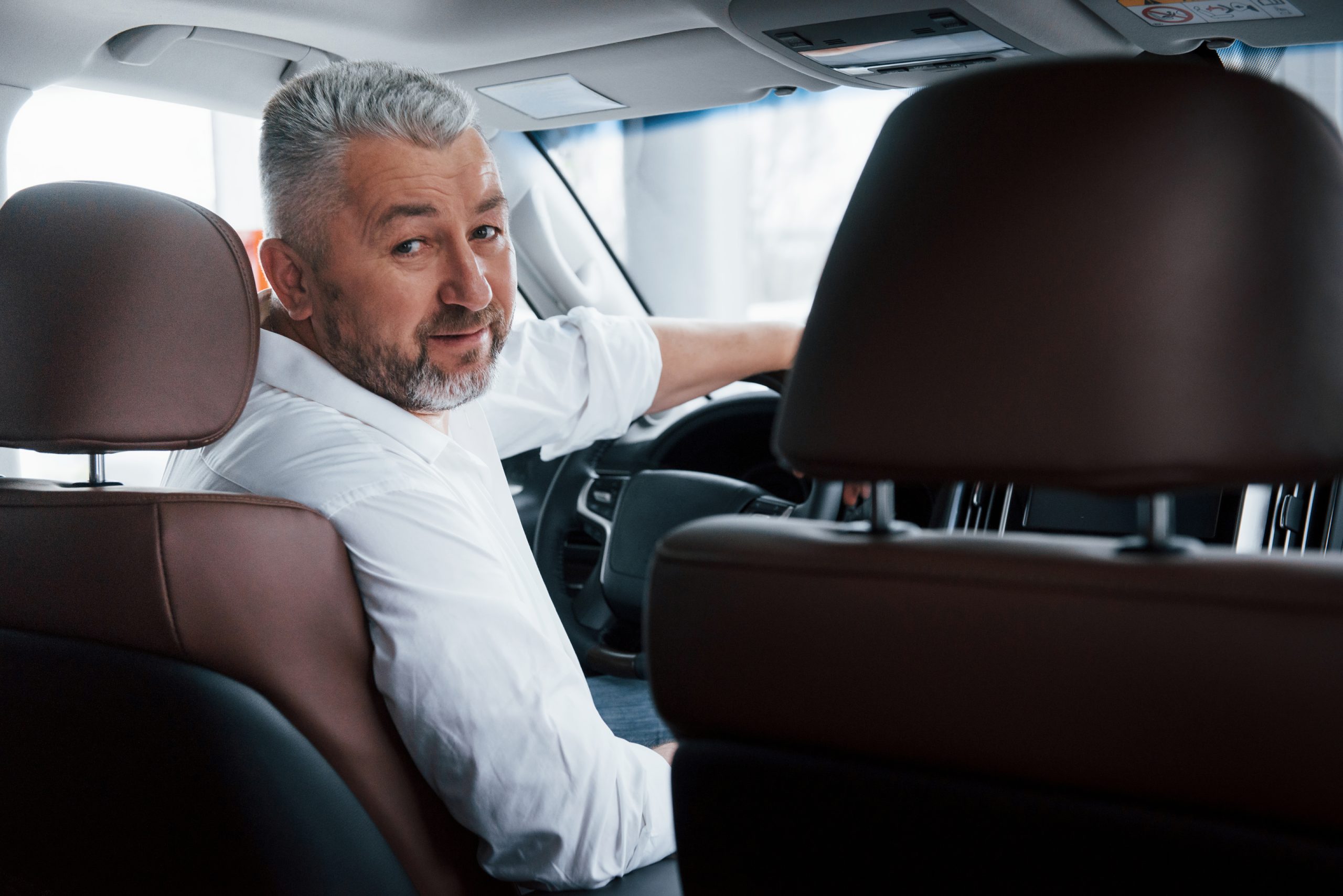 conception of success joyful bearded man in white shirt looks back while sitting in the modern car scaled